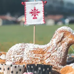 Baranek wielkanocny, symbol ofiarowania i nowego życia, w otoczeniu babeczek i zieleni.