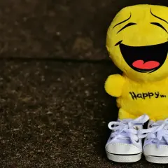 Żółta maskotka z napisem "Happy..." na brzuchu i uśmiechem od ucha do ucha. Idealna, by przypomnieć o cytatach, które poprawiają humor.
