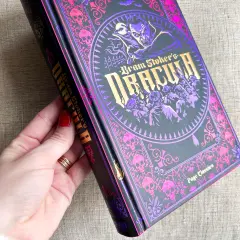 Dłoń trzyma ozdobną książkę z wampirem i czaszkami. To "Dracula" Brama Stokera, autora tej mrocznej opowieści.
