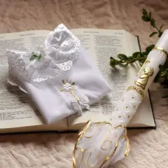 Biała szatka i paschalna świeca na otwartej Biblii. Symbole chrztu i ich znaczenie, światło wiary i czystość.
