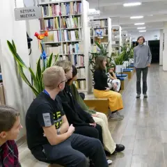 Grupa osób słucha opowieści o tym, że kto czyta książki żyje podwójnie, autor opowieści stoi w tle.