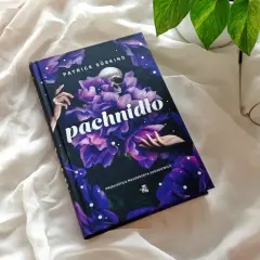 Recenzja książki "Pachnidło" Patricka Süskinda. Na zdjęciu okładka z czaszką i kwiatami, obok okulary i otwarta książka.