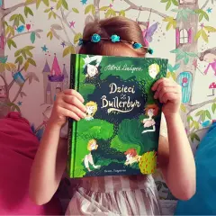 Dziecko z książką "Dzieci z Bullerbyn", której autorem jest Astrid Lindgren, na tle bajkowej tapety.