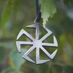 Metalowy symbol Słońca, jeden z wielu symbole słowiańskie znaczenie. Wisi na sznurku wśród zielonych liści.