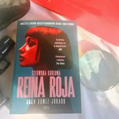 Recenzja książki "Czerwona Królowa" Juana Gómeza-Jurado. Obok leży pistolet i lupa, sugerując kryminalną fabułę.