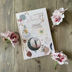 Recenzja książki "Oskar i Pani Róża" na tle drewnianych desek, ozdobiona delikatnymi kwiatami.