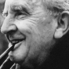 J.R.R. Tolkien, autor książki Hobbit, pali fajkę, uśmiechając się.