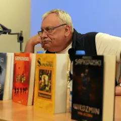 Andrzej Sapkowski, autor książki Wiedźmin, siedzi obok swoich dzieł.