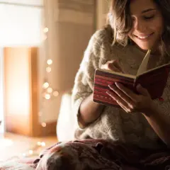 Uśmiechnięta kobieta czyta w notesie, łapiąc ulotne chwile jak motyle. Cytaty w jej dłoniach.
