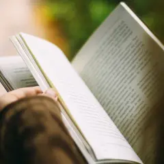 Otwarta książka w dłoni, strony pełne tekstu. Czytanie to podróż, która inspiruje i pokazuje, dlaczego warto czytać książki, cytaty z nich są jak skarby.