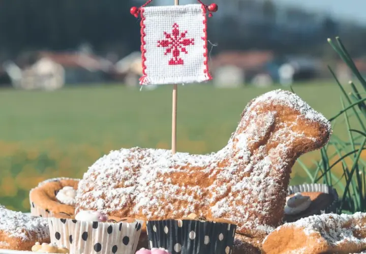 Baranek wielkanocny, symbol ofiarowania i nowego życia, w otoczeniu babeczek i zieleni.