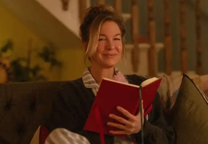 Bridget Jones uśmiecha się, czytając książkę. To idealny moment na recenzję książki "Dziennik Bridget Jones".