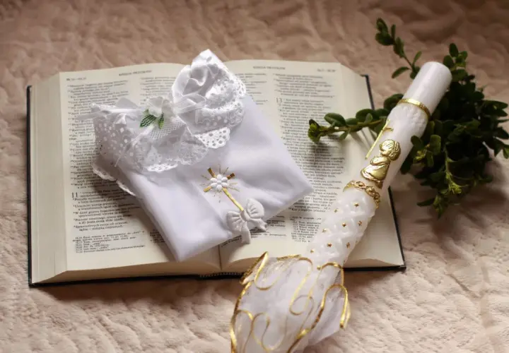 Biała szatka i paschalna świeca na otwartej Biblii. Symbole chrztu i ich znaczenie, światło wiary i czystość.