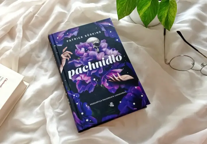 Recenzja książki "Pachnidło" Patricka Süskinda. Na zdjęciu okładka z czaszką i kwiatami, obok okulary i otwarta książka.