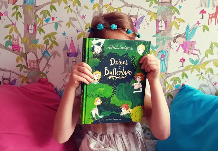 Dziecko z książką "Dzieci z Bullerbyn", której autorem jest Astrid Lindgren, na tle bajkowej tapety.