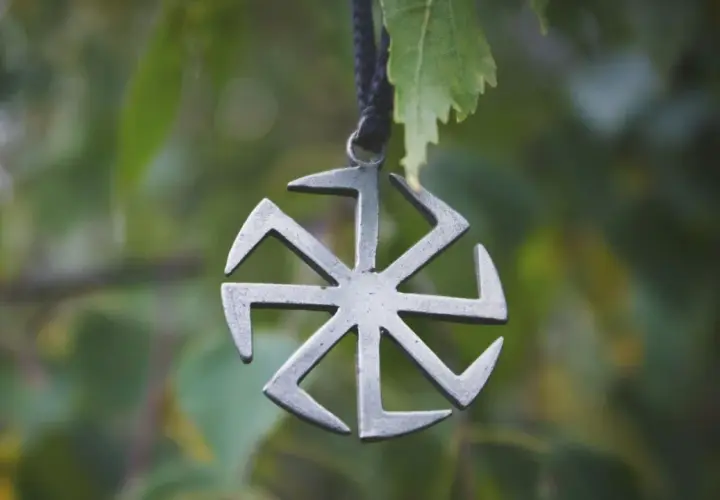 Metalowy symbol Słońca, jeden z wielu symbole słowiańskie znaczenie. Wisi na sznurku wśród zielonych liści.