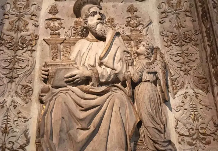 Rzeźba przedstawia św. Mateusza z aniołem, symbolizując znaczenie symboli ewangelistów. W tle widoczne ornamenty.