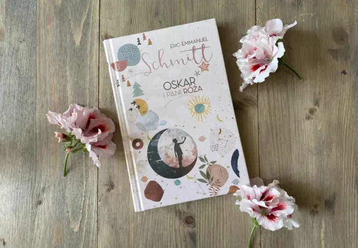 Recenzja książki "Oskar i Pani Róża" na tle drewnianych desek, ozdobiona delikatnymi kwiatami.