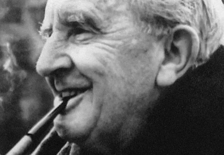 J.R.R. Tolkien, autor książki Hobbit, pali fajkę, uśmiechając się.
