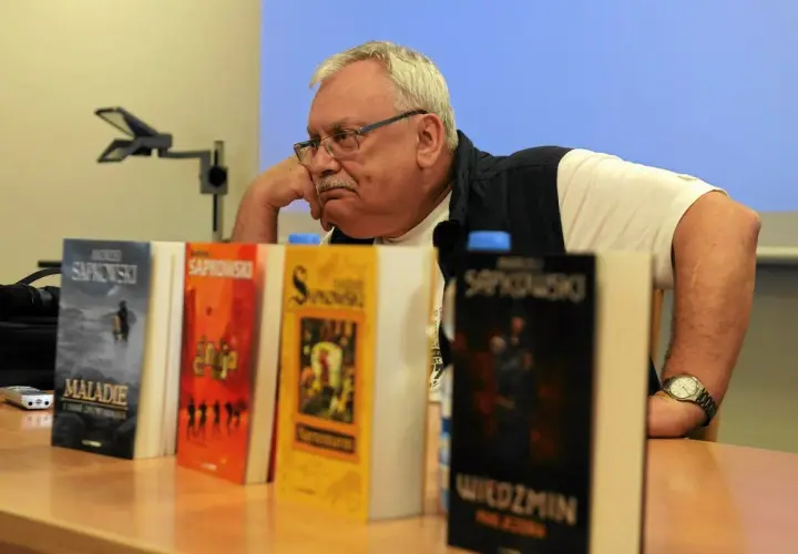 Andrzej Sapkowski, autor książki Wiedźmin, siedzi obok swoich dzieł.