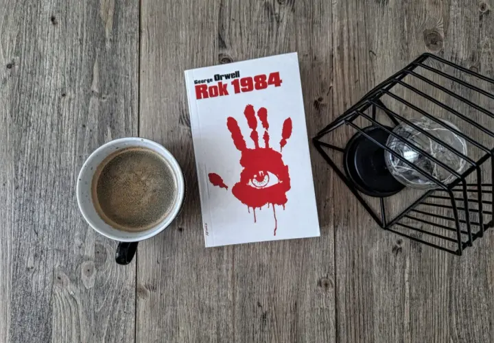 Kawa i książka "Rok 1984" George'a Orwella na drewnianym stole. Recenzja tej ponadczasowej lektury czeka.