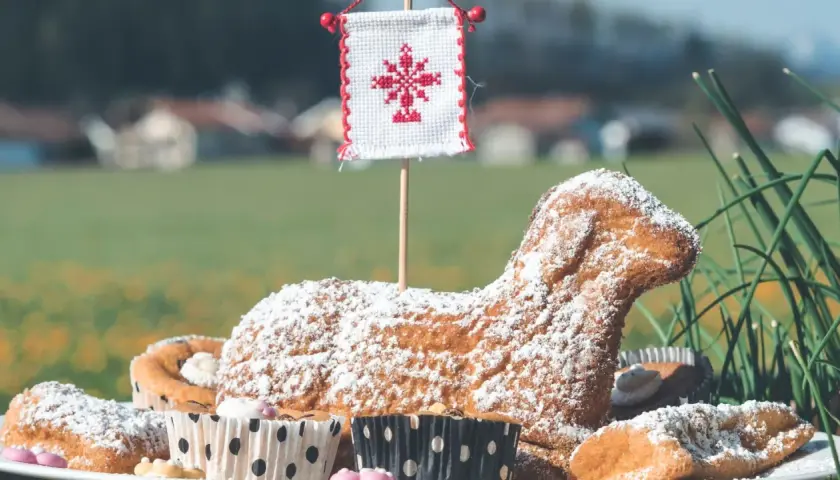 Baranek wielkanocny, symbol ofiarowania i nowego życia, w otoczeniu babeczek i zieleni.