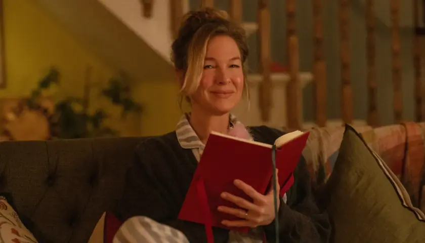 Bridget Jones uśmiecha się, czytając książkę. To idealny moment na recenzję książki "Dziennik Bridget Jones".