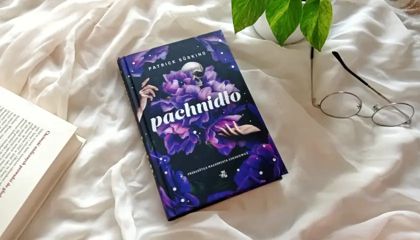 Recenzja książki "Pachnidło" Patricka Süskinda. Na zdjęciu okładka z czaszką i kwiatami, obok okulary i otwarta książka.