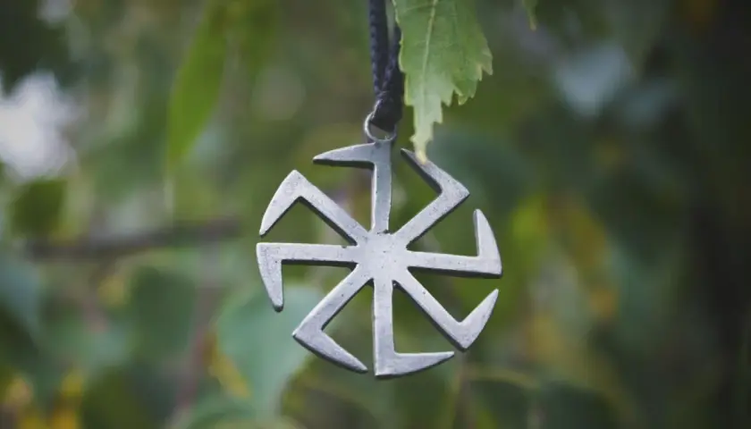 Metalowy symbol Słońca, jeden z wielu symbole słowiańskie znaczenie. Wisi na sznurku wśród zielonych liści.
