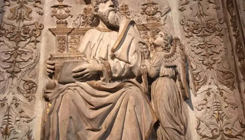 Rzeźba przedstawia św. Mateusza z aniołem, symbolizując znaczenie symboli ewangelistów. W tle widoczne ornamenty.