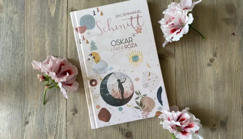 Recenzja książki "Oskar i Pani Róża" na tle drewnianych desek, ozdobiona delikatnymi kwiatami.