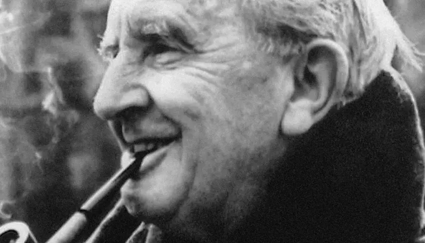 J.R.R. Tolkien, autor książki Hobbit, pali fajkę, uśmiechając się.