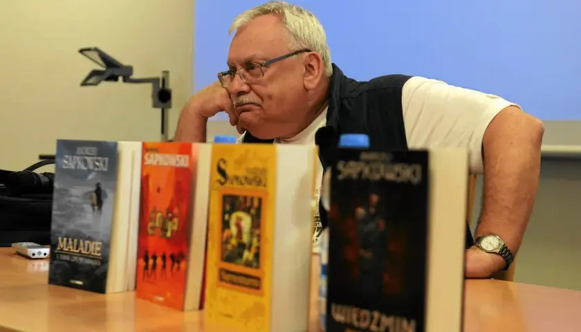 Andrzej Sapkowski, autor książki Wiedźmin, siedzi obok swoich dzieł.