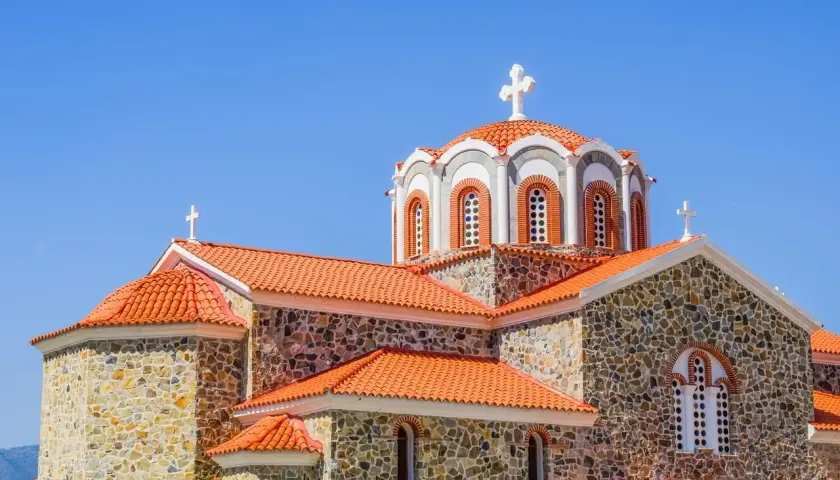 Kamienna cerkiew z pomarańczowym dachem i krzyżami na kopułach. Symbolika religijna i ich znaczenie widoczne w architekturze.