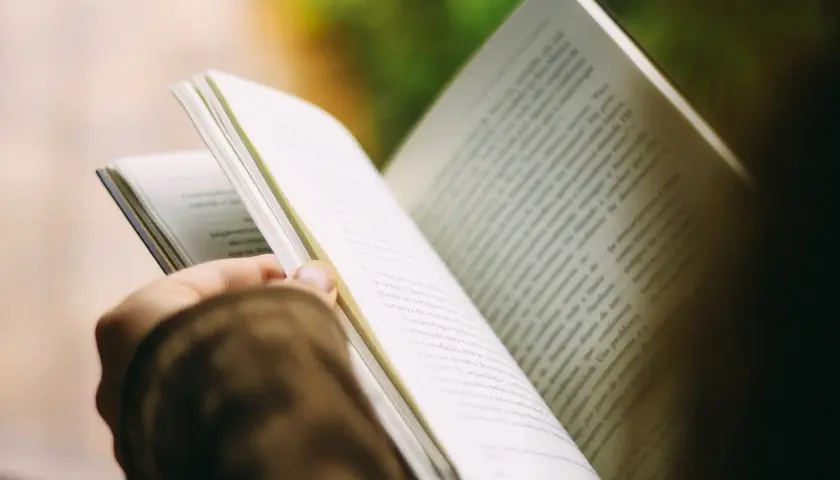 Otwarta książka w dłoni, strony pełne tekstu. Czytanie to podróż, która inspiruje i pokazuje, dlaczego warto czytać książki, cytaty z nich są jak skarby.