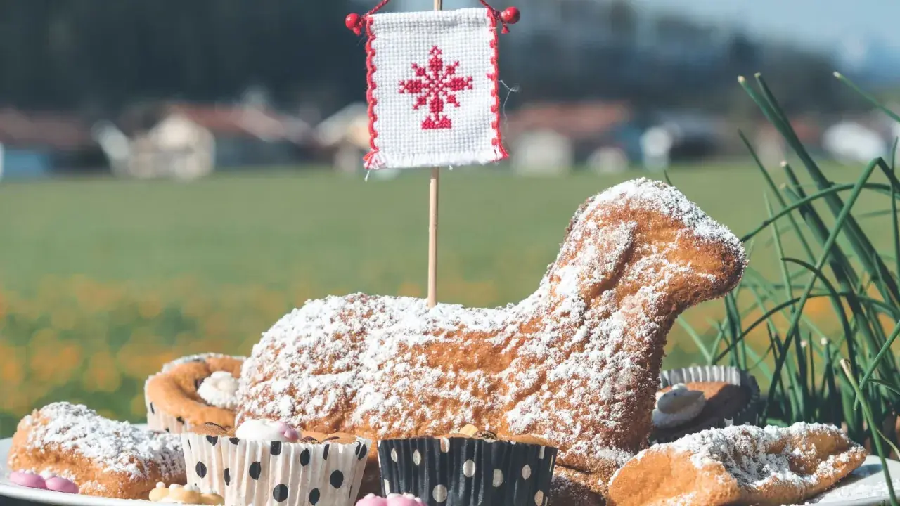 Baranek wielkanocny, symbol ofiarowania i nowego życia, w otoczeniu babeczek i zieleni.
