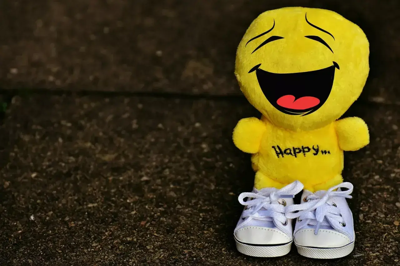 Żółta maskotka z napisem "Happy..." na brzuchu i uśmiechem od ucha do ucha. Idealna, by przypomnieć o cytatach, które poprawiają humor.