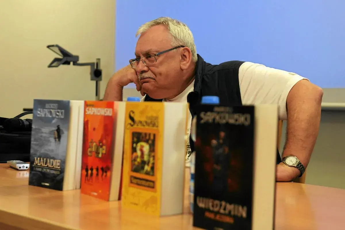 Andrzej Sapkowski, autor książki Wiedźmin, siedzi obok swoich dzieł.