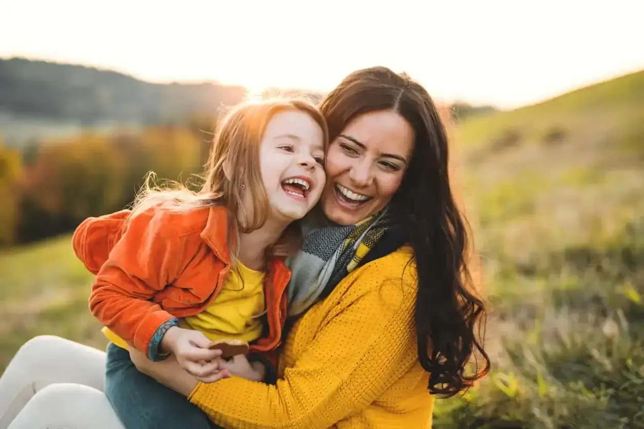 Uśmiechnięta mama i córka przytulają się na tle jesiennego krajobrazu. Ich radość potwierdza, że jaka matka taka córka cytaty.